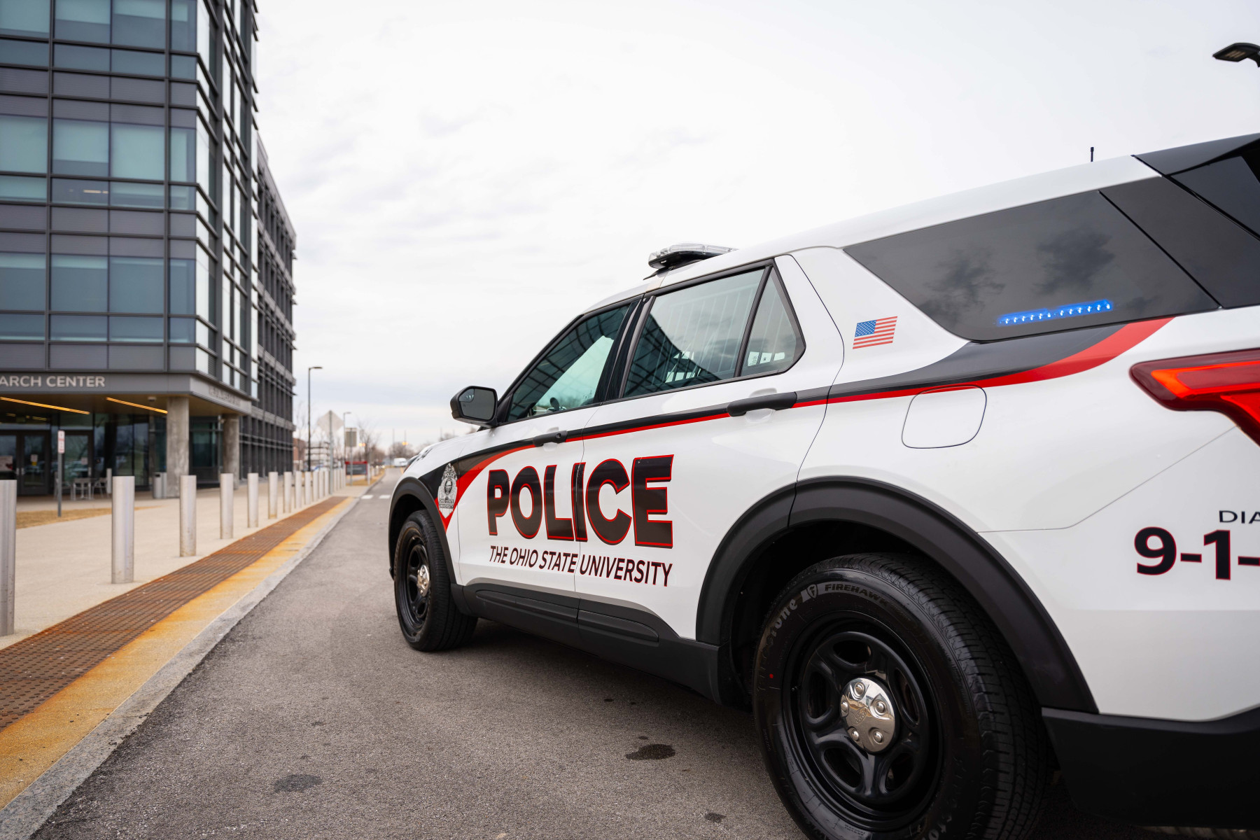 OSUPD Vehicle with blue lights on in the back, side window.