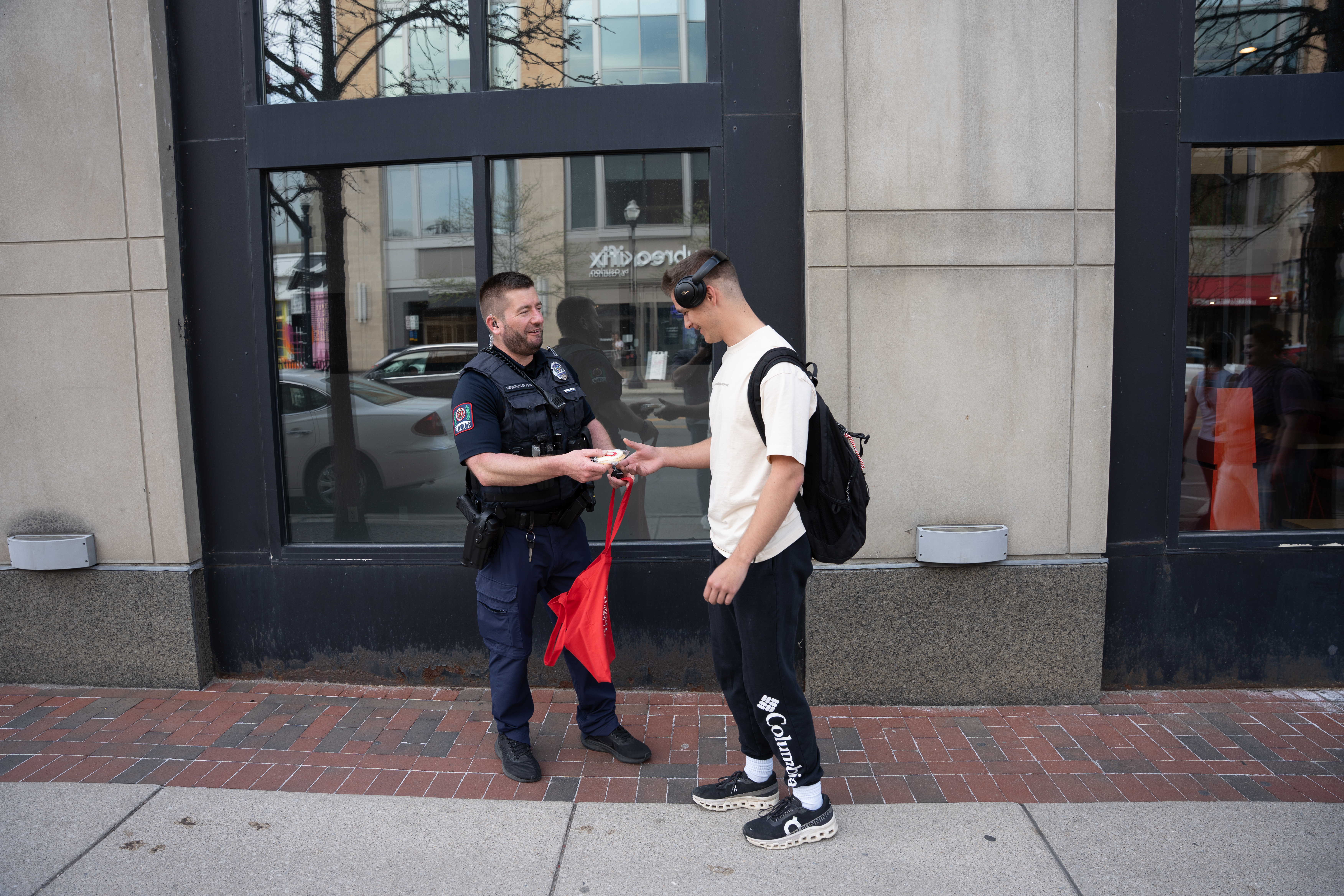 A police officer and student smile at each other while they officer hands the student something.