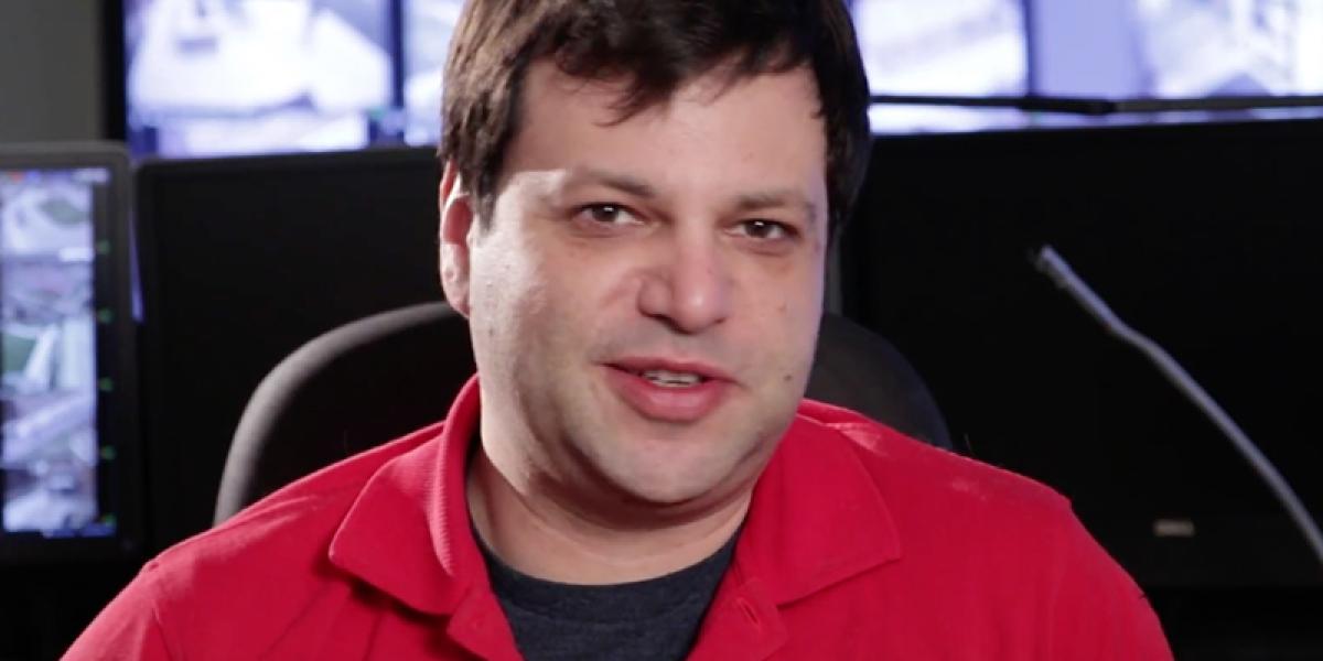 Alex sitting at his desk, with security monitors in the background