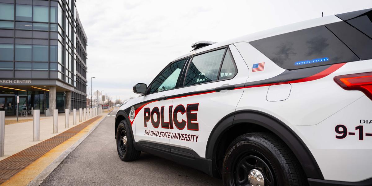 OSUPD Vehicle with blue lights on in the back, side window.