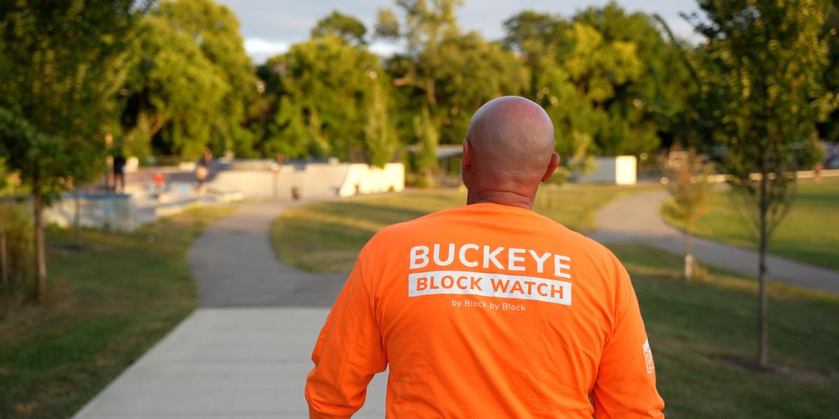 A view of a man walking with a neon shirt on that says, "Buckeye Block Watch"