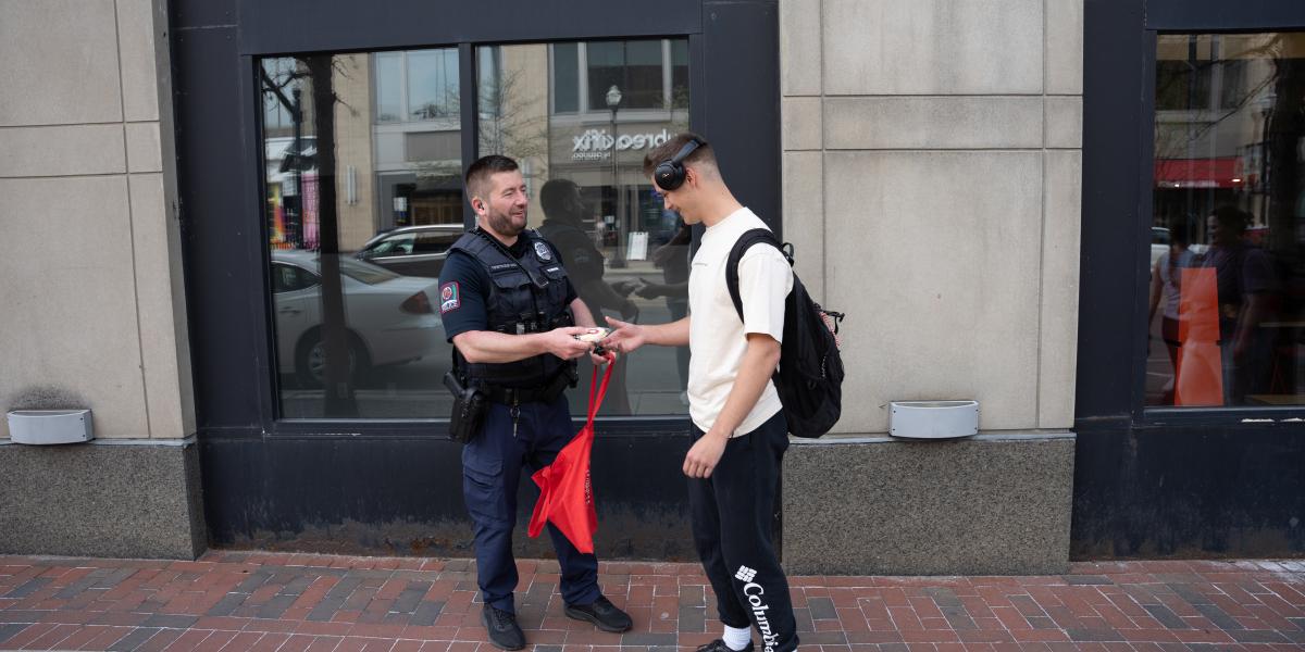 A police officer and student smile at each other while they officer hands the student something. 