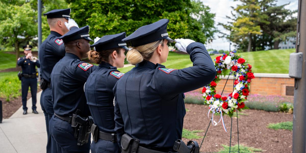 Four officers salute a flower wreath.