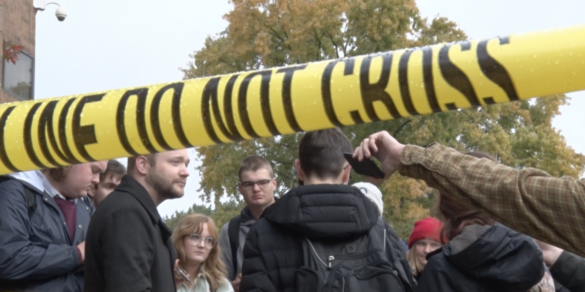 Do Not Cross yellow caution tape frames student journalists in the background