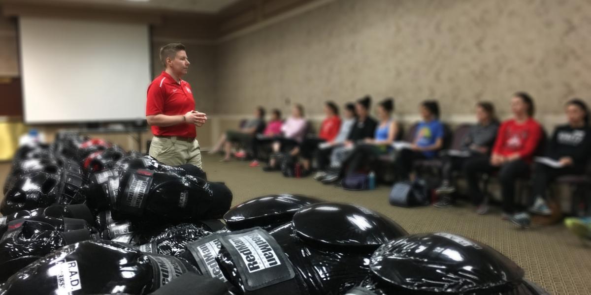 officer standing next to self-defense training gear, talking to students