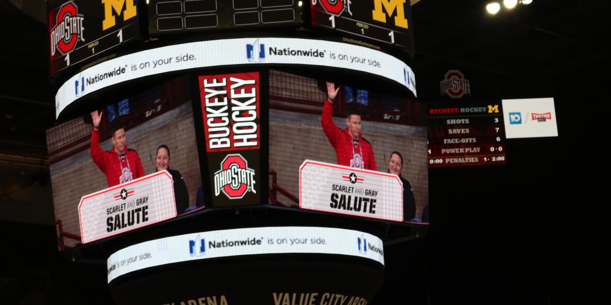 central display board about the ice at the hockey game, displaying Officer Shaffer waving to acknowledge the applause