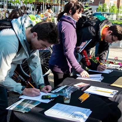 several students at an event table, leaning over and filling out bug your bike registration forms