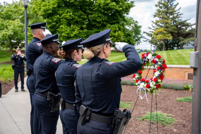 Four officers salute a flower wreath.