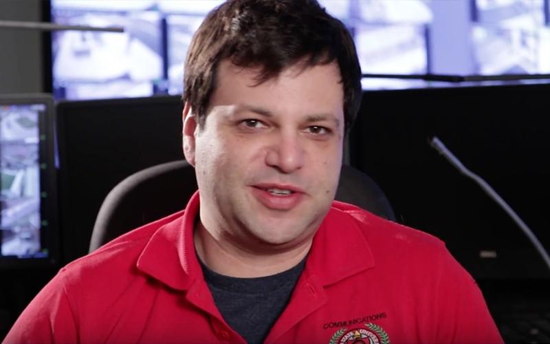 Alex sitting at his desk, with security monitors in the background