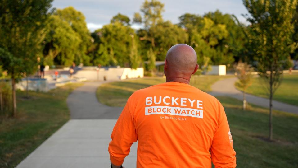 A view of a man walking with a neon shirt on that says, "Buckeye Block Watch"