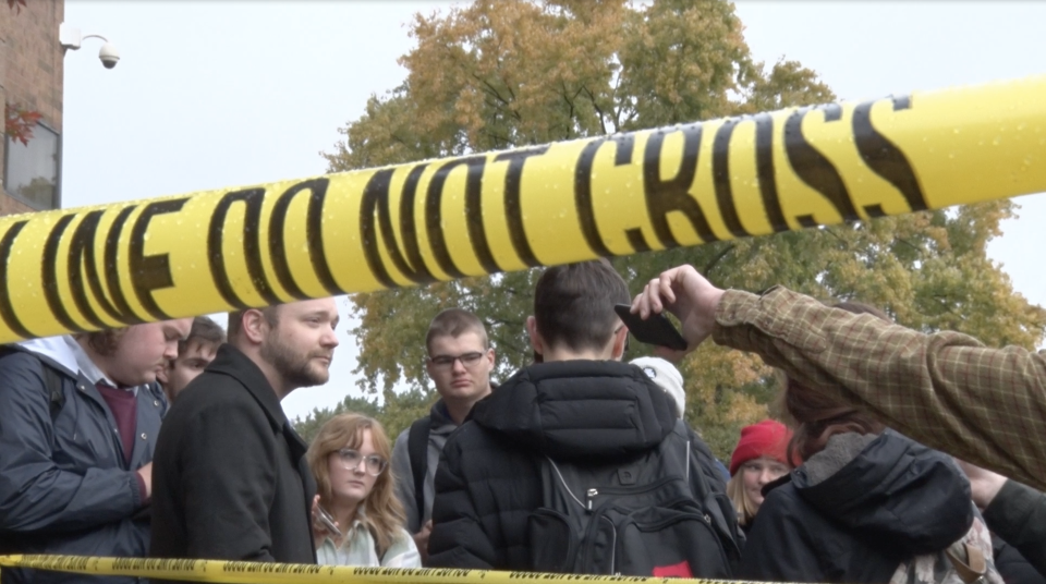Do Not Cross yellow caution tape frames student journalists in the background