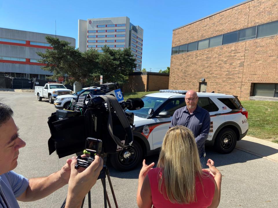 reporter interviews man on camera in front of police car